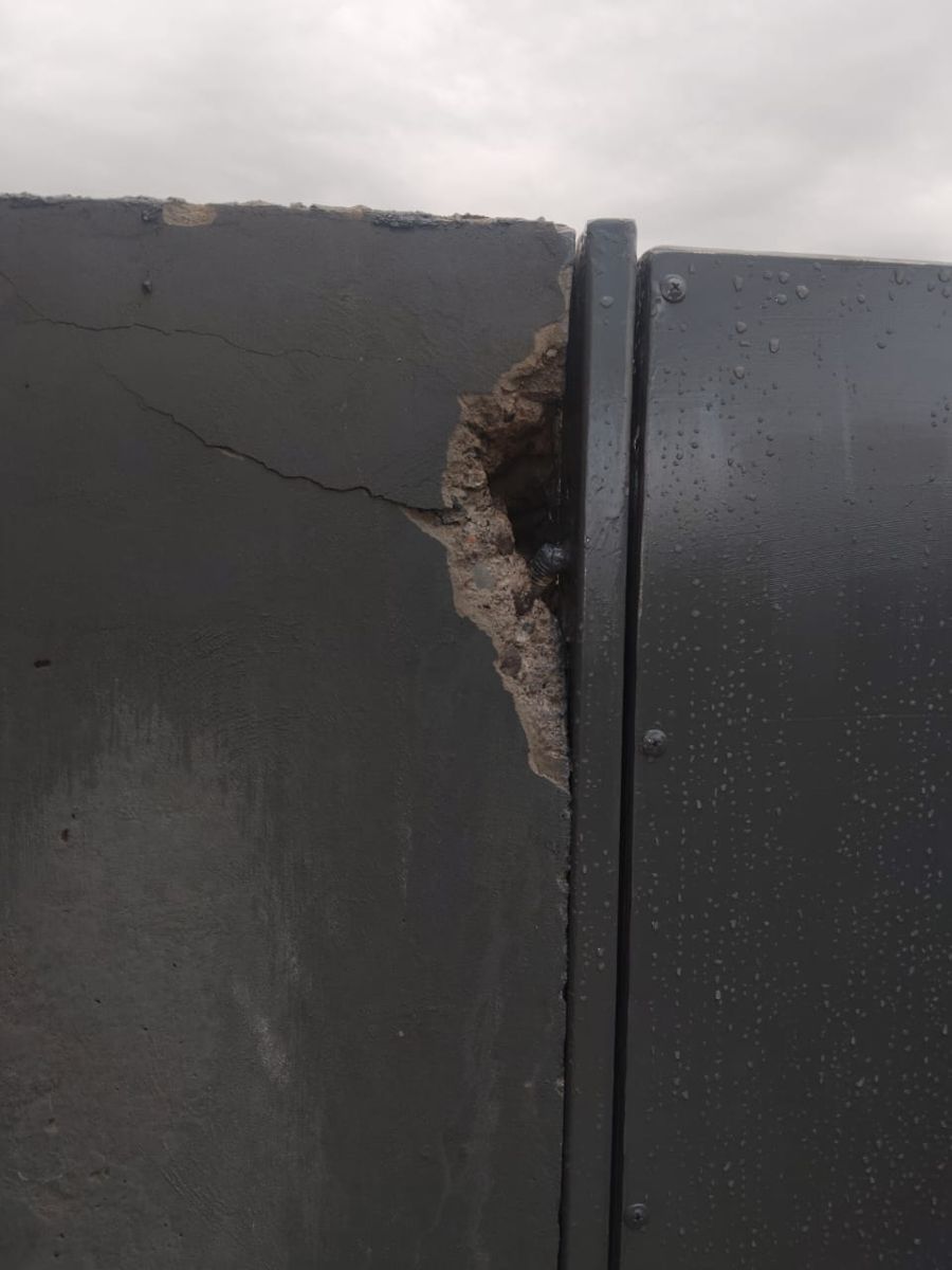 Muro de hormigón quebrado junto al marco de un portón, con la fijación a la vista